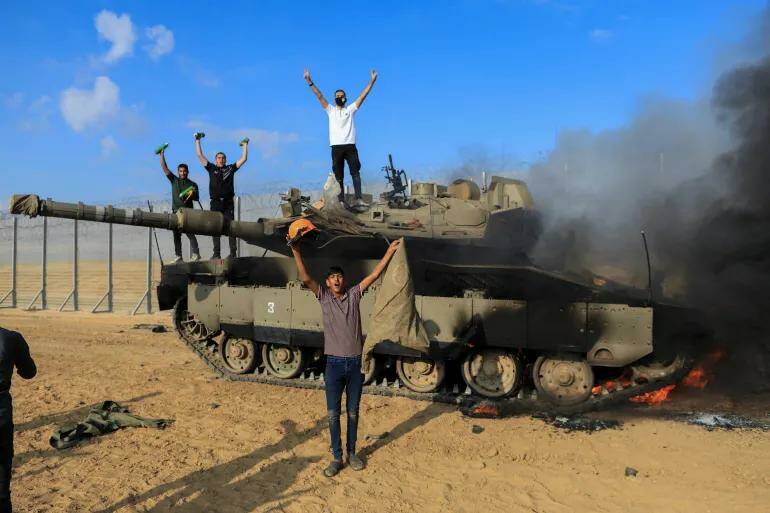 Палестинцы празднуют на израильской стороне израильско-газинской границы, где горит израильский танк после нападения палестинских боевиков